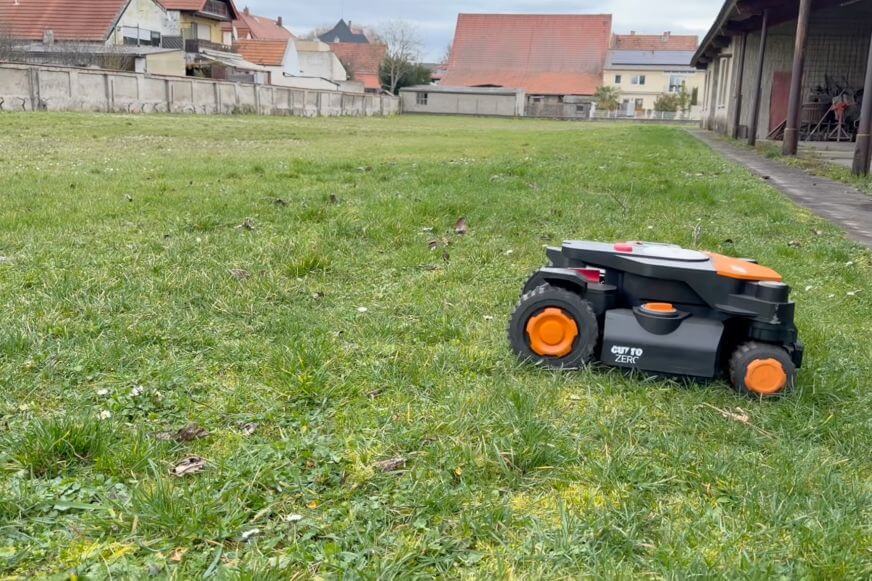 Mähroboter fährt über eine Bodenwelle auf unebenem Rasen und man sieht das dynamische Fahrwerk